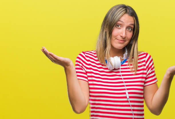 young beautiful woman listening music wearing headphones over isolated background clueless and confused expression with arms and hands raised. doubt concept. - head and shoulders audio imagens e fotografias de stock