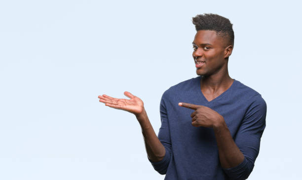 istock Young african american man over isolated background amazed and smiling to the camera while presenting with hand and pointing with finger. 1050848288