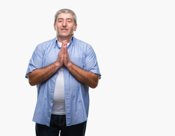 istock Handsome senior man over isolated background praying with hands together asking for forgiveness smiling confident. 1050859020