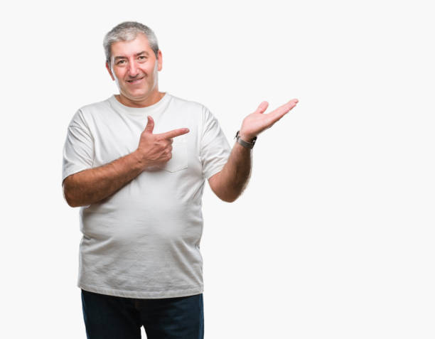 istock Handsome senior man over isolated background amazed and smiling to the camera while presenting with hand and pointing with finger. 1050859472