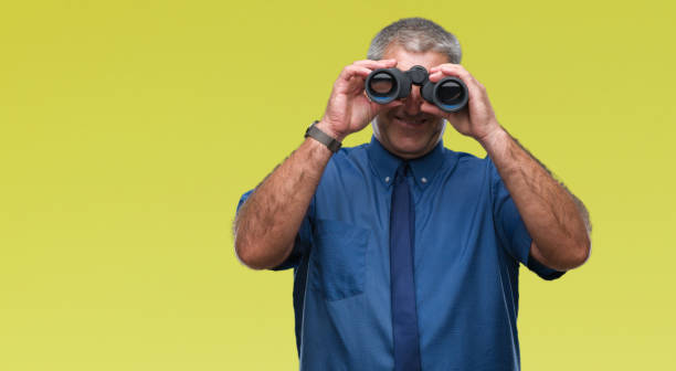 istock Handsome senior man looking through binoculars over isolated background with a happy face standing and smiling with a confident smile showing teeth 1050863010