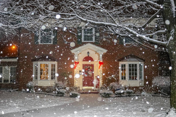 istock Snowfall on beautiful brick house with columns and bay windows with Christmas tree light up and red sled and wreath on porch 1050863608