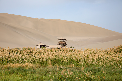 Wooden pagoda on Crescent Lake in marshes with landscape of Singing Sand Mountain dunes of Taklamakan Desert, Dunhuang, China.