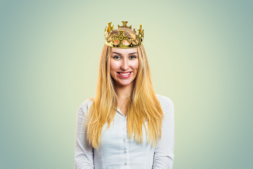 Smiling self-confident blond woman in golden crown and white shirt looking at camera