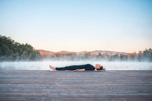 Shot of young woman doing yoga in nature on a misty morning in Ljubljana, Slovenia. Foggy lake is in the back.