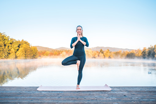 Shot of young woman doing yoga in nature on a misty morning in Ljubljana, Slovenia. Foggy lake is in the back.