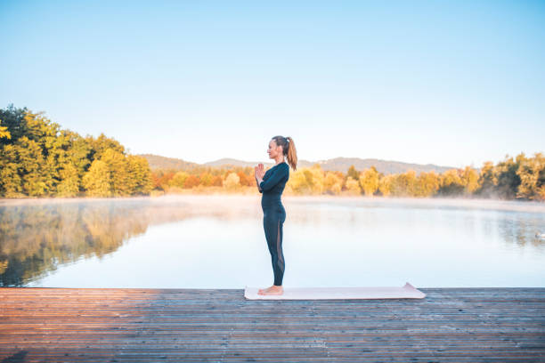 Shot of young woman doing yoga in nature on a misty morning in Ljubljana, Slovenia. Foggy lake is in the back.