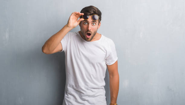 istock Handsome young man over grey grunge wall wearing sunglasses afraid and shocked with surprise expression, fear and excited face. 1050889206