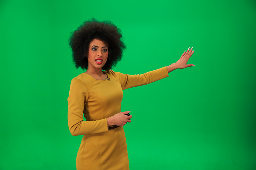 Young weather woman in front of a green background with small remote in her other hand.