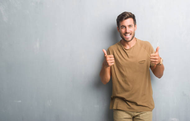 istock Handsome young man over grey grunge wall success sign doing positive gesture with hand, thumbs up smiling and happy. Looking at the camera with cheerful expression, winner gesture. 1050891704