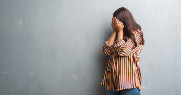 istock Young brunette woman over grunge grey wall with sad expression covering face with hands while crying. Depression concept. 1050895346
