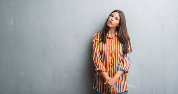 istock Young brunette woman over grunge grey wall making fish face with lips, crazy and comical gesture. Funny expression. 1050895374