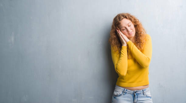 istock Young redhead woman over grey grunge wall sleeping tired dreaming and posing with hands together while smiling with closed eyes. 1050895778