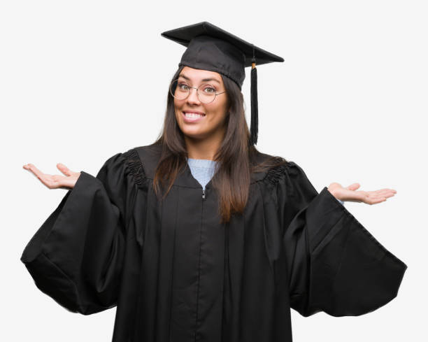 istock Young hispanic woman wearing graduated cap and uniform clueless and confused expression with arms and hands raised. Doubt concept. 1050898798