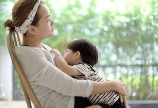 Little asian boy feeds on mother's breasts milk : Soft focus stock photo