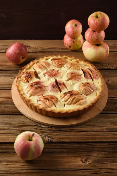 Rustic apple pie with cream filling served with organic apples on old wooden table. Homemade autumn sweet dessert