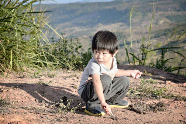 Child boy drawing into sand with a wood stick