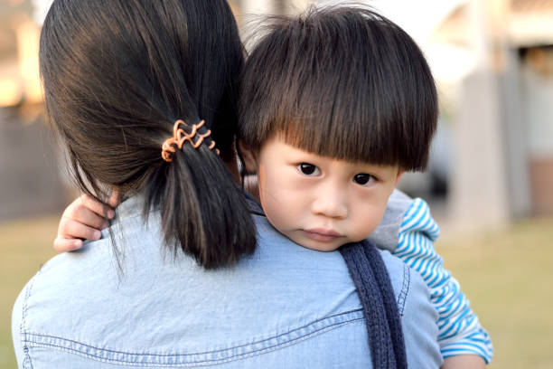 Young boy looking over mother's shoulder stock photo