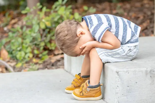 Sad male toddler covering his face with his hands