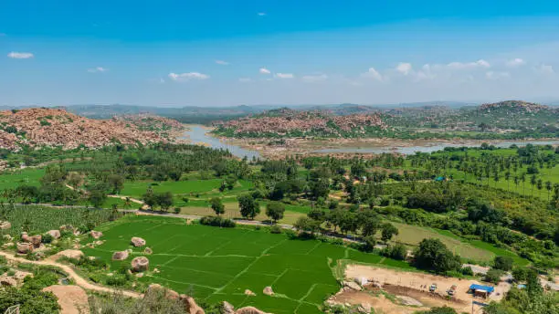 Photo of Bright green paddy fields against a backdrop of rocky hills and the tungabhadra river in the distance in Hampi India