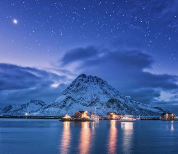 雪に覆われた山々 と、ノルウェーのロフォーテン諸島の夜の月と星空紫海の桟橋付近の漁船。船、建物、照明、岩、雲のある冬景色 - fishing village nordic countries fjord ストックフォトと画像