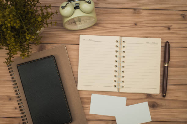 istock Office supplies or office work essential tools items on wooden desk in workplace, pen with notebook and alarm clock, top view 1050964876