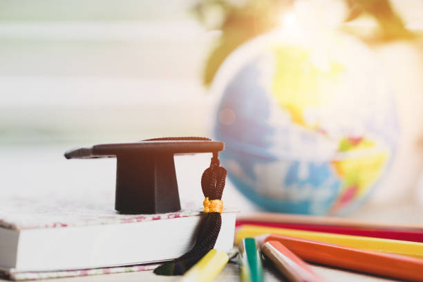 istock Graduate or Education knowledge learning study abroad concept : Graduation cap on book with blur of america earth world globe, with color pencils on wood floor. Work and travel. Back to School 1050970724