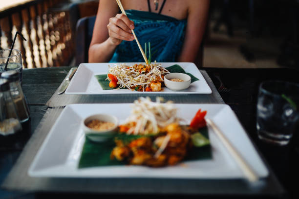 Young woman enjoying a delicious pad thai with seafood and vegetables in a beach bar on the Koh Phangan island, Thailand.
