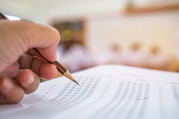 istock Students hands taking exams, writing examination room with holding pencil on optical form of standardized test with answers and english paper sheet on row desk chair doing final exam in classroom. 1050973100