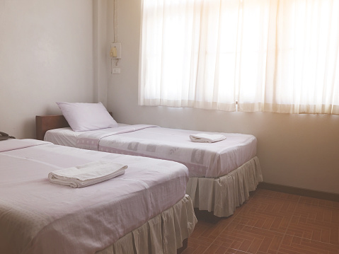 Generic bedroom interior of two single beds with sun light through window at cheap hotel.