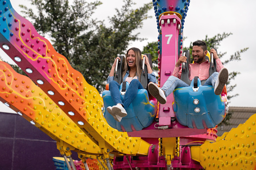 Happy couple having fun in an amusement park riding on a fun ride and laughing - lifestyle concepts