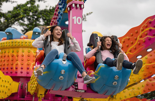 Happy girls having fun in an amusement park riding on a fun ride and screaming - lifestyle concepts