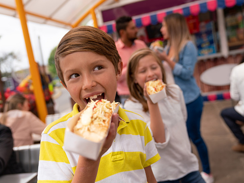 Portrait of happy kids eating junk food at an amusement park and smiling - lifestyle concepts