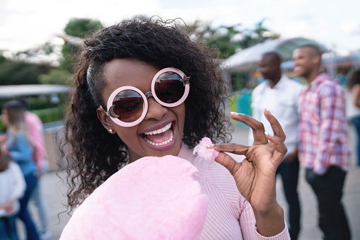 Portrait of a happy woman eating a cotton candy at an amusement park and wearing fun glasses - lifestyle concepts