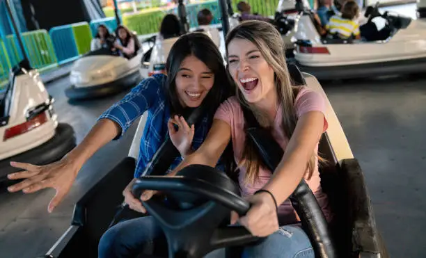 Two happy women having fun on the bumper cars at an amusement park - lifestyle concepts