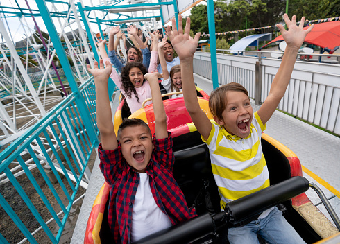 Very happy kids having fun on a rollercoaster at an amusement park and screaming with arms up - lifestyle concepts
