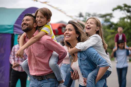 Portrait of a happy family having fun at an amusement park and carrying kids on a piggyback ride - lifestyle concepts