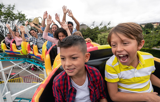 Happy kids having fun in an amusement park riding on a rollercoaster and screaming - lifestyle concepts