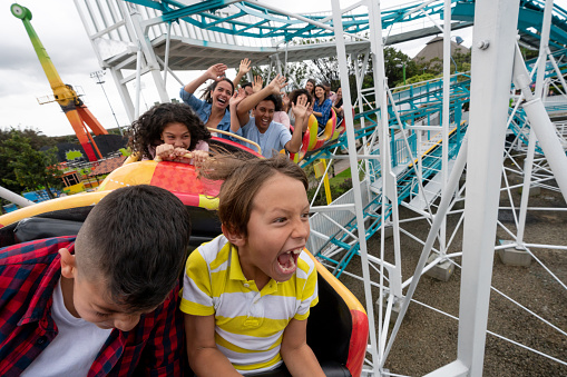 Excited group of people having fun riding on a rollercoaster in an amusement park - lifestyle concepts