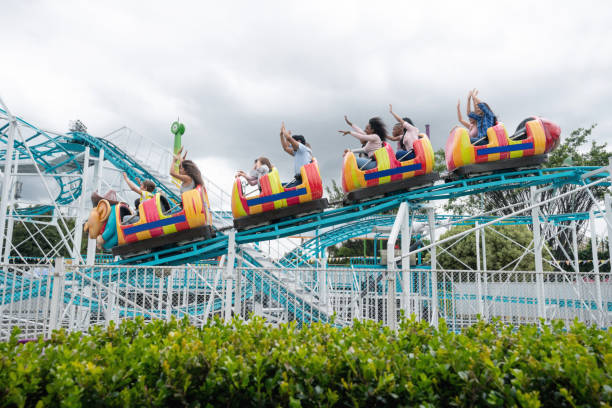 Happy group of people having fun in an amusement park riding on a rollercoaster with arms up - lifestyle concepts