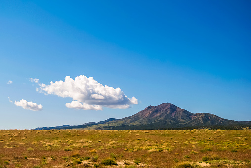 In the desert of western Utah, this small peak rises sharply from the vast fields of sage and grasses in the arid landscape. Above, a small cloud forms near the peak in the otherwise clear blue sky.