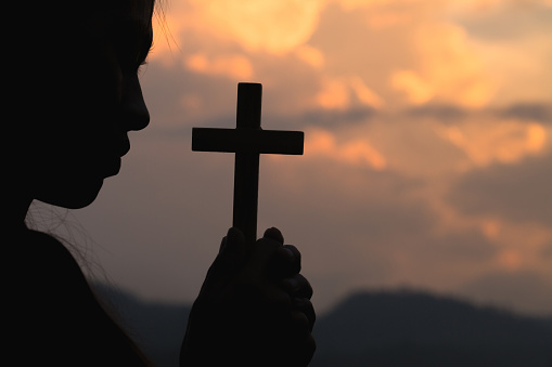 Silhouette off woman hands holding wooden cross  on sunrise background, Crucifix, Symbol of Faith.