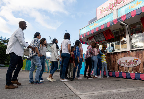 Happy people at a funfair buying food at the candy shop - lifestyle concepts