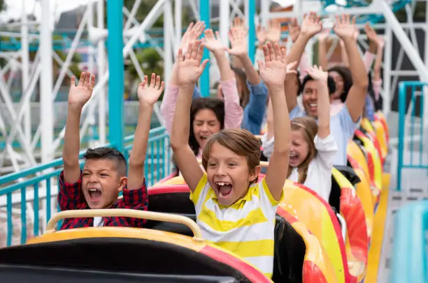 Happy group of people having fun in an amusement park riding on a rollercoaster with arms up and screaming - lifestyle concepts