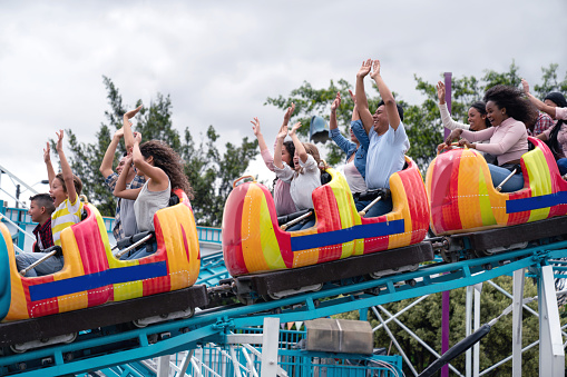 Happy group of people having fun in an amusement park riding on a rollercoaster with arms up - lifestyle concepts