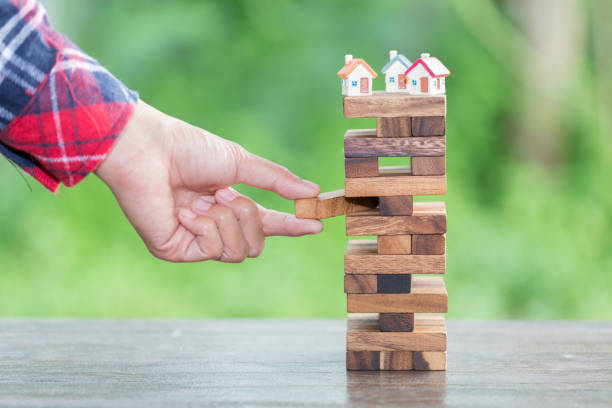 A hand placing a piece of jenga to the stack with two houses on top