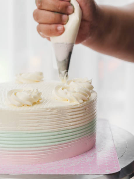 istock Confectioner topping cakes with cream using a pastry bag, 1051018486