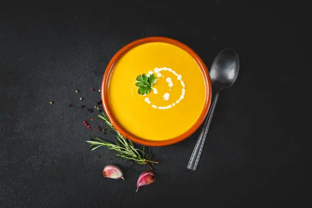 Pumpkin Cream soup on black board background. Autumn yellow cream-soup in country style. Top view.
