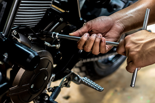 Image is close up. People holding hand are repairing a motorcycle Use a wrench and a screwdriver to work.