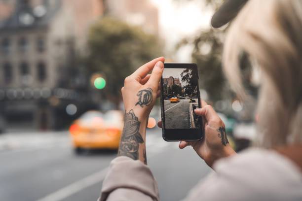 Female tourist in New York taking photos with phone A tattooed woman is a tourist in New York, taking photos with her smart phone. photo messaging stock pictures, royalty-free photos & images